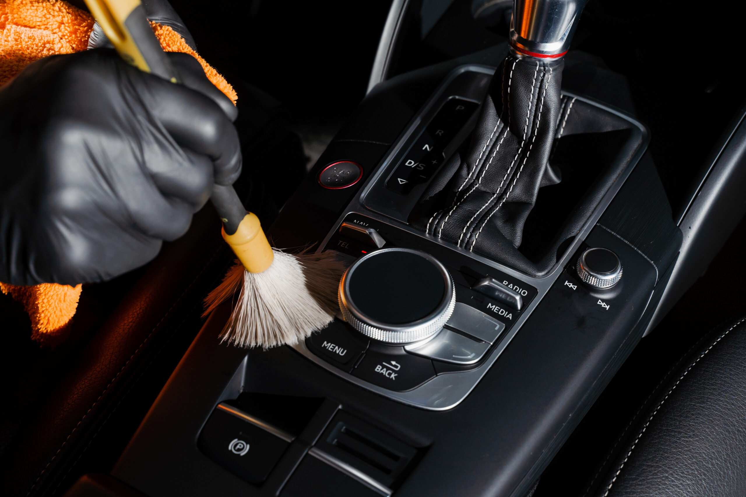 Dry cleaning with brush of gearbox and dashboard in car. Auto detailing service. Cleaning individual elements of black leather interior in auto